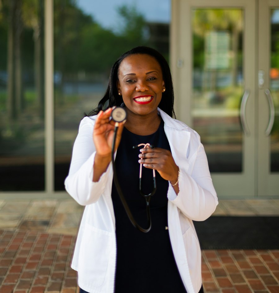 A smiling Black female doctor in a white coat holding a stethoscope